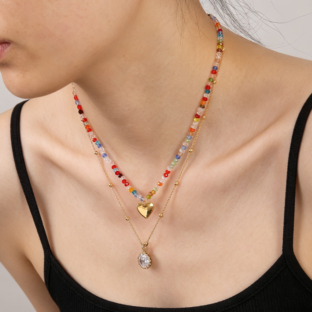 Woman wearing double layer rainbow crystal beaded necklace with gold heart charm and oval crystal pendant on black top