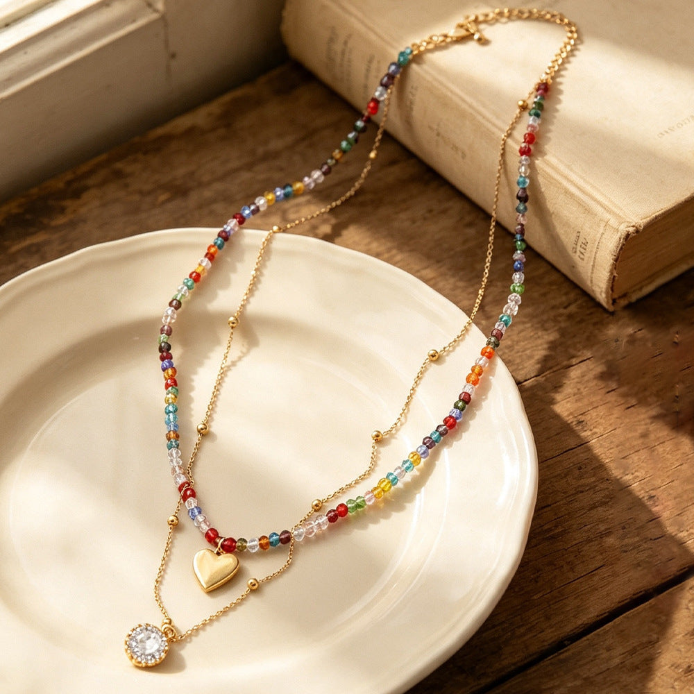 Woman wearing double layer rainbow crystal beaded necklace with gold heart charm and oval crystal pendant on black top