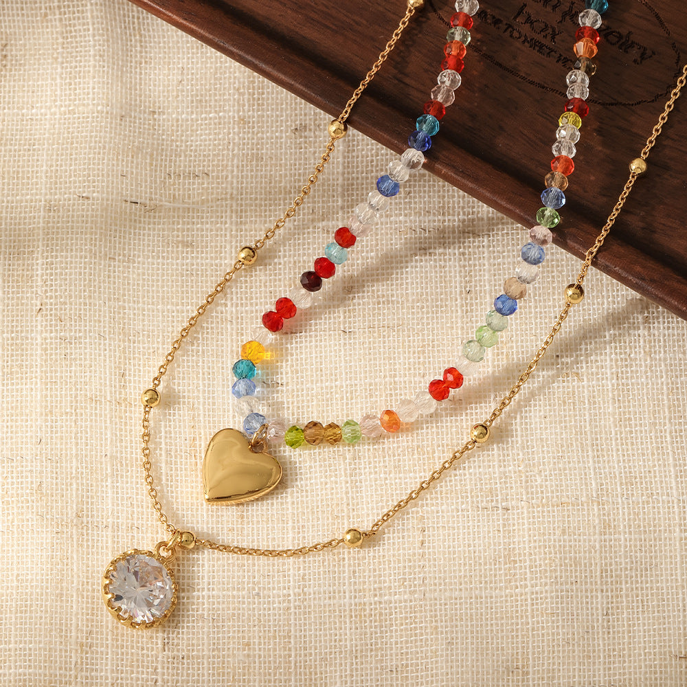 Woman wearing double layer rainbow crystal beaded necklace with gold heart charm and oval crystal pendant on black top